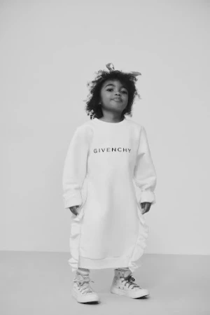 Child wearing white sweatshirt dress and high top sneakers standing against a seamless light background