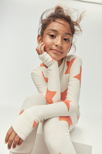 Young girl with long hair poses while wearing a star-patterned shirt and pants in a close-up studio shot on a white background.