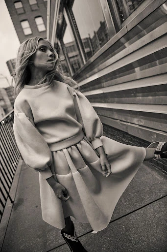 Monochrome shot of a blonde woman in a pastel sweater dress walking in an urban setting, showcasing fashion and street style.