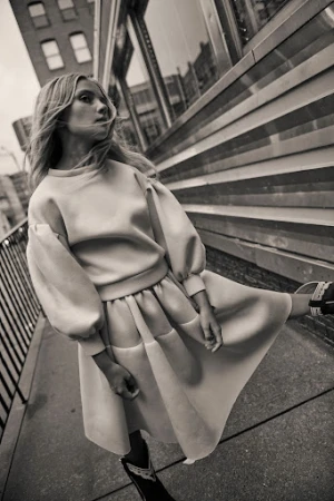 Monochrome shot of a blonde woman in a pastel sweater dress walking in an urban setting, showcasing fashion and street style.