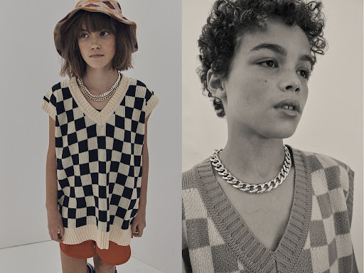 Two children, one wearing a hat, are pictured in a split-screen studio shot, both wearing silver necklaces and checkered sweater vests.