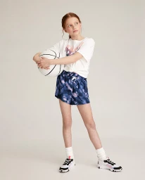 Young girl holding a white basketball wearing a white t-shirt and patterned blue shorts on a seamless background