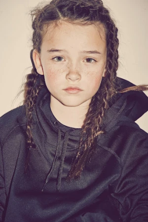 Close-up portrait of a child with braided hair wearing a black hooded sweatshirt against a plain white background