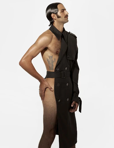 Adult male fashion model poses bare-chested in an open, dark-grey trench coat against a white background, side lit.