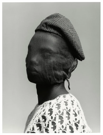 Monochrome portrait of a person wearing a plaid driving cap and a sheer fabric over their face, with a Dior logo shirt.