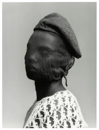 Monochrome portrait of a person wearing a plaid driving cap and a sheer fabric over their face, with a Dior logo shirt.