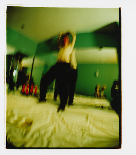 Blurred action shot of a person jumping on a bed in a green room, captured with motion blur and a vintage aesthetic.