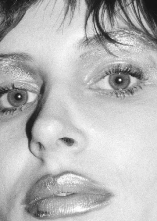 Close-up portrait of a woman with metallic makeup, dark bangs, and textured monochrome grain.