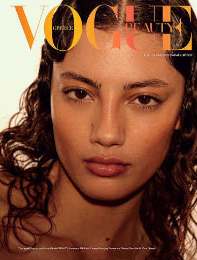 Close-up of a model with wet, wavy hair and glossy lips against a clean backdrop, featured on the cover of Vogue Greece Beauty magazine.