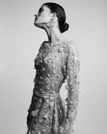 Monochrome portrait of a model in profile wearing a textured lace dress and large statement earrings.