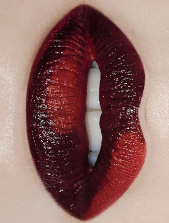 Close-up macro shot of dark burgundy glossy lipstick on lips with a slight gap revealing white teeth