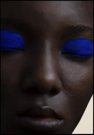Close-up beauty portrait of a Black woman with vibrant blue eyeshadow and closed eyes, styled by Yvane Rocher