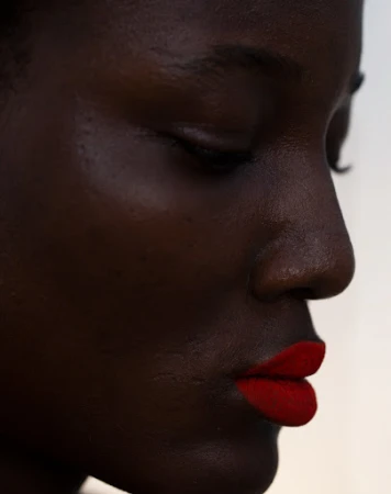 Close-up portrait of a Black woman with closed eyes and vibrant red lipstick against a plain white background