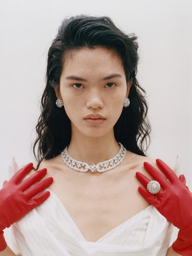 Glamorous woman wearing diamond jewelry and red gloves against a bright white background in a fashion portrait shot.