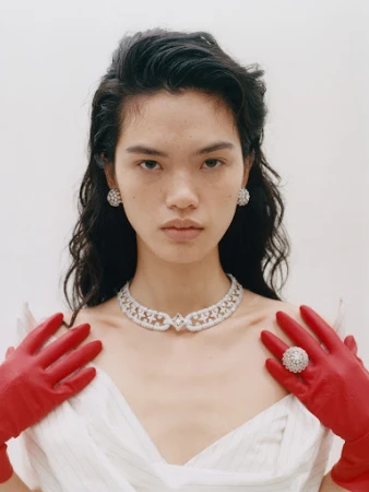 Glamorous woman wearing diamond jewelry and red gloves against a bright white background in a fashion portrait shot.