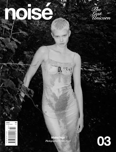 Black and white magazine cover shot of a fashion model in a transparent dress standing in front of foliage and trees.
