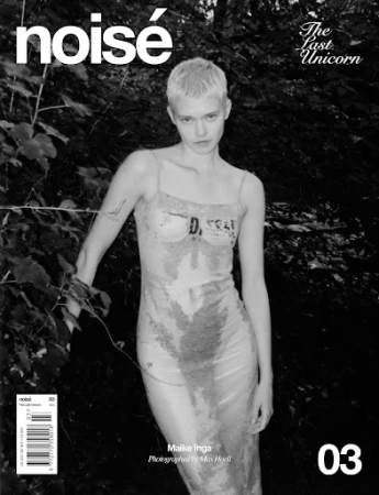 Black and white magazine cover shot of a fashion model in a transparent dress standing in front of foliage and trees.