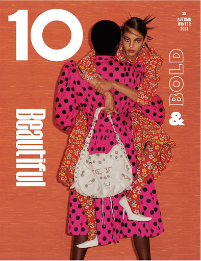Two models wearing patterned clothing embracing against an orange background with bold white typography.