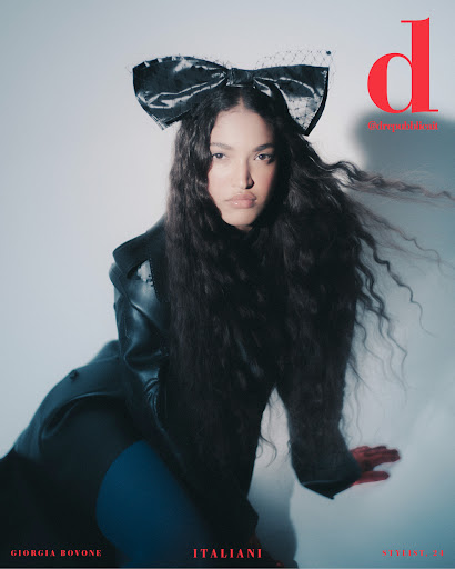 Fashion magazine cover featuring a woman with long, wavy hair wearing a large black bow and a black leather jacket against a light background.
