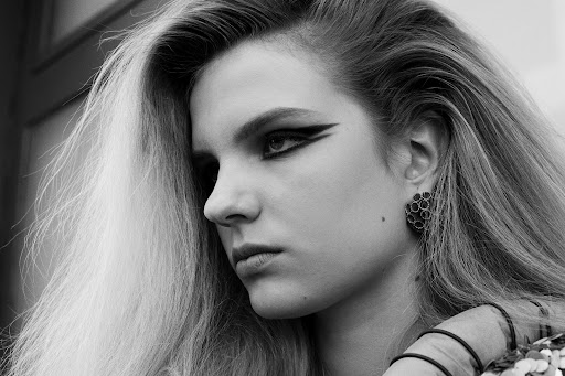 Close-up monochrome portrait of a woman with dramatic winged eyeliner and voluminous blonde hair, styled by Andrea Lemme.