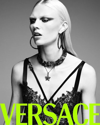 Monochrome portrait of a fashion model wearing a black bra top and statement jewellery, shot against a gray background.