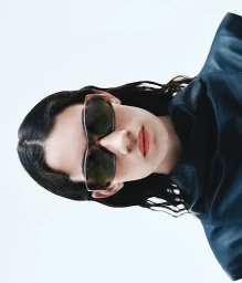Portrait of a woman wearing tortoiseshell sunglasses and a dark top against a white background, styled by Andrea Lemme.