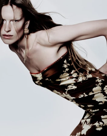 Model in strapless floral dress with long gold pendant earring posing against a light background
