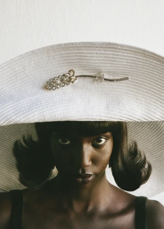 Black woman wearing a wide white brimmed hat with a jewelled brooch and dark dress by Bastien Zorzetto
