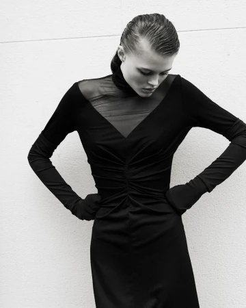 Black and white portrait of a fashion model with wet hair and a black, form-fitting dress posing against a plain white background.