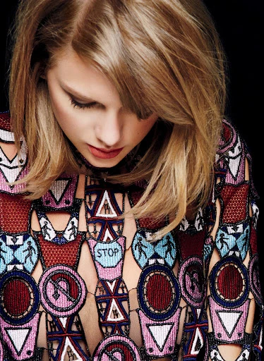 Portrait of a blonde woman with fair skin wearing a patterned top, against a dark background in a studio setting. Fashion, beauty.