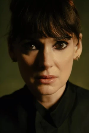 Close-up portrait of a woman with dark hair and bangs wearing a black top against a dark textured background.