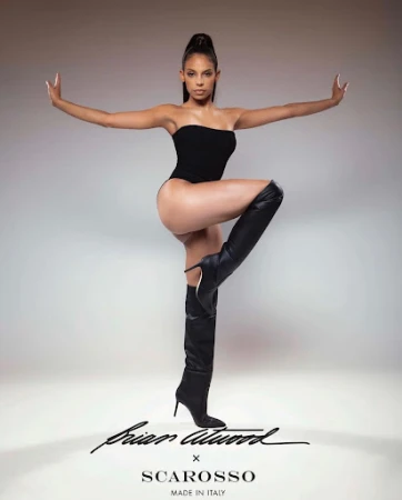 Woman in a black strapless bodysuit and knee-high leather boots posing against a neutral gradient backdrop
