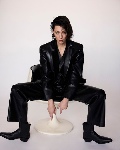 Woman in a black leather suit seated in a white pod chair against a seamless background