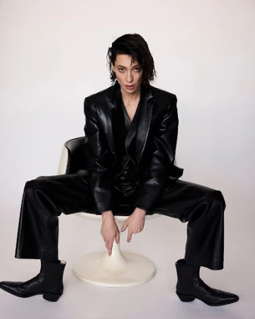 Woman in a black leather suit seated in a white pod chair against a seamless background