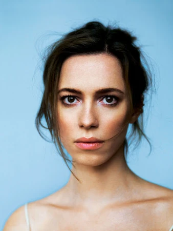 Close-up portrait of a woman with dark hair and neutral expression against a solid blue background