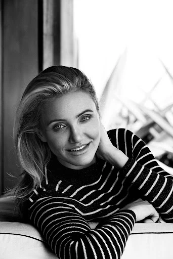 Black and white portrait of a blonde woman in a striped shirt, looking at the camera with a relaxed smile in an indoor setting.