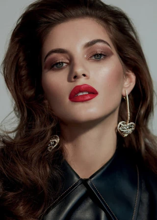 Close-up portrait of a woman with bold red lipstick, dark leather jacket, and ornate heart-shaped drop earrings by Ben Skervin.