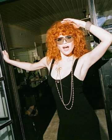 Woman with curly red hair and tinted sunglasses wearing a black dress by Ben Skervin
