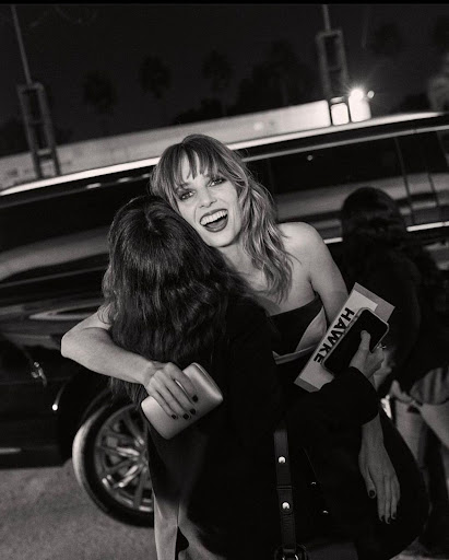 Black and white photograph of Maya Hawke hugging a fan on the street, with a car visible in the background at night.