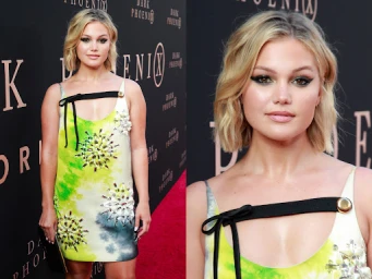 Olivia Holt with short blonde wavy hair wearing a yellow and green printed dress on a red carpet in Los Angeles