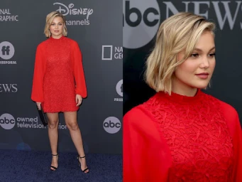 Olivia Holt wearing a red mini dress and black heels on a blue carpet against a branded dark backdrop.