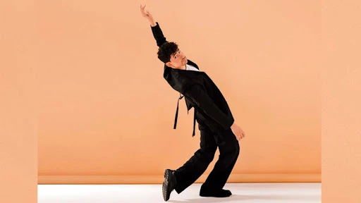 A male model poses in a photo studio wearing a green jacket, shirt, and pants, complemented by brown boots, set against a neutral background.
