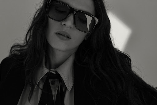 Close-up portrait of a woman wearing dark sunglasses and a collared shirt with hair styled by Carlos Ferraz.