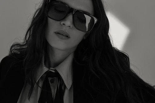 Close-up portrait of a woman wearing dark sunglasses and a collared shirt with hair styled by Carlos Ferraz.