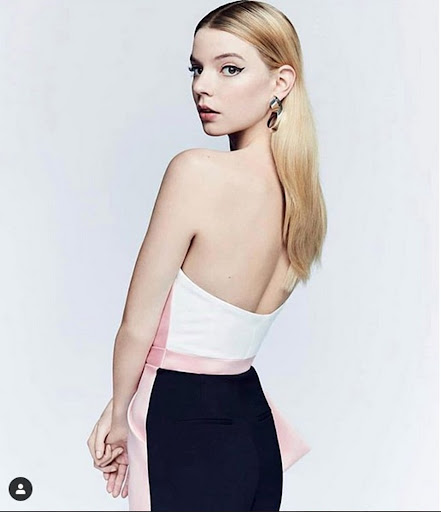 Blonde woman in a strapless top and black pants looking back over her shoulder, posing against a white backdrop in a studio setting.