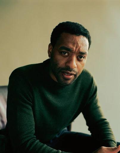 Portrait of actor Chiwetel Ejiofor in an olive green sweater, seated against a neutral backdrop in a studio setting with natural lighting.