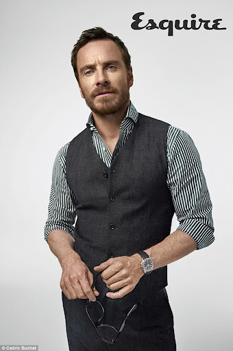 Portrait of a handsome adult man in a vest and striped shirt, holding glasses, against a neutral background with an Esquire logo.