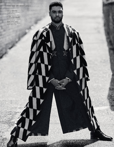 Man in black and white patterned coat stands in alleyway with confident pose, showcasing fashion in an urban outdoor setting.