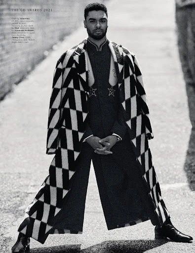 Man in black and white patterned coat stands in alleyway with confident pose, showcasing fashion in an urban outdoor setting.