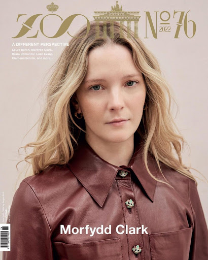 Close-up portrait of Morfydd Clark with blonde hair wearing a dark brown leather shirt against a neutral background.
